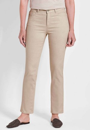 Beige Jeans mit schlankem Schnitt, hoher Taille und subtiler Textur. Kombiniert mit dunklen, geflochtenen Mules, die einen lässigen Eindruck vermitteln.