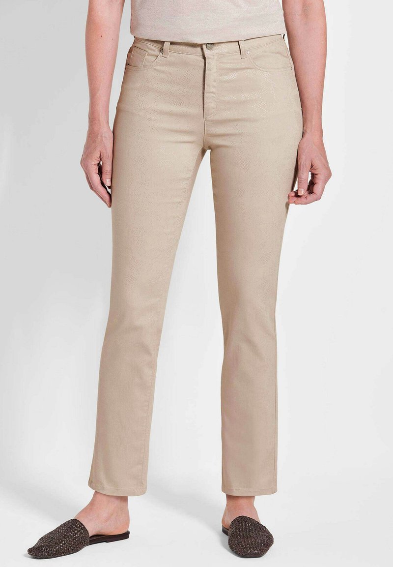 Beige Jeans mit schlankem Schnitt, hoher Taille und subtiler Textur. Kombiniert mit dunklen, geflochtenen Mules, die einen lässigen Eindruck vermitteln.