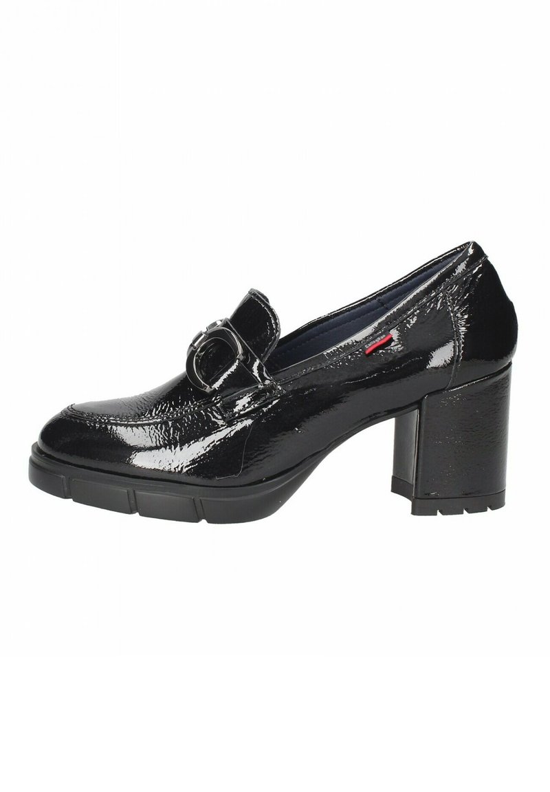 Zapato de charol negro de tacón alto con punta redondeada, que presenta un gran detalle de hebilla circular en el empeine y un tacón grueso y texturizado.