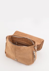 Torebka crossbody w kolorze jasnobeżowym z klapą, wyposażona w liczne zasuwane kieszenie oraz srebrne akcenty metalowe. Gładka faktura, prostokątny kształt.