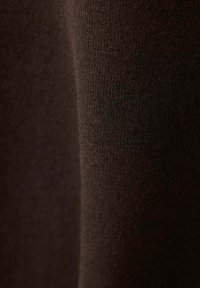 Gros plan d'un tissu tricoté marron foncé montrant une texture fine et régulière ainsi que le détail du matériau doux.