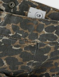 Tissu en denim au motif camouflage dans des nuances de gris et de marron, avec une fermeture à bouton et une étiquette blanche. Texturé et robuste.