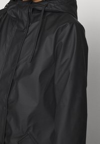 Schwarze, wasserdichte Jacke mit Kapuze, Kordeln und einer schlanken, glatten Textur sowie einer Detailtasche auf der Vorderseite.