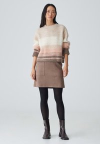Gestrickter Pullover mit einem Farbverlauf in hellrosa, creme und braun; kombiniert mit einem braunen Wildlederrock mit zwei vorderen Taschen; schwarze Strumpfhosen und braune Stiefel.