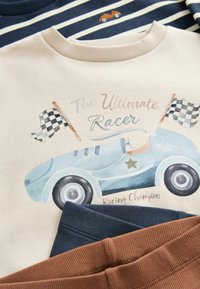 Sudadera crema con un coche de carreras vintage azul, banderas a cuadros y el texto "El Campeón de Carreras Definitivo", combinada con pantalones azules y marrones.