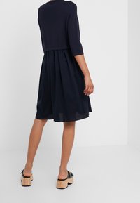 Abito blu navy con corpetto aderente e gonna a campana, caratterizzato da maniche a tre quarti e una cintura testurizzata. Indossato con scarpe con tacco in sughero.