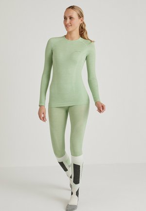 Lichtgroene basislaagtop en leggings van textuurstof, met een aansluitend ontwerp en naadloze constructie. Versterkt door ribbeldetails.
