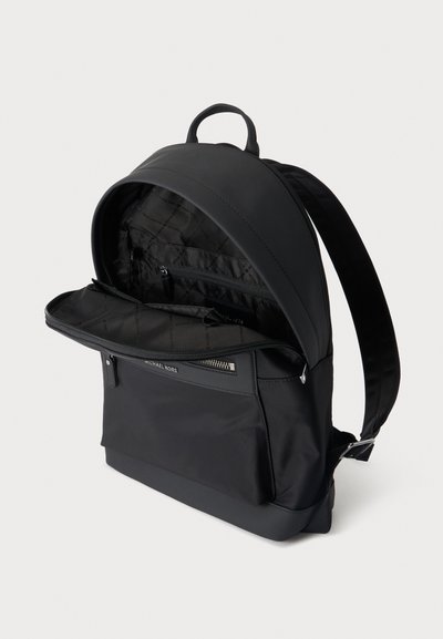 Sac à dos noir Michael Kors avec compartiment principal ouvert montrant des poches intérieures et des bretelles rembourrées sur un fond uni.