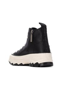 Zapatilla alta de cuero negro con suela gruesa blanca, cierre con cremallera y acentos texturizados. Cuenta con una lengüeta en el talón para facilitar su uso.