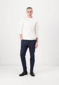 Light textured sweater in cream, paired with dark navy fitted trousers and black ankle boots. Minimalist design with a modern fit.