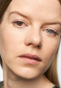 Close-up van een gezicht met een egale huid, lichtbruin haar, één bruine oog en één blauwe oog, natuurlijke make-up en lichtroze lippen.