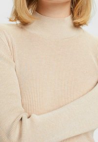 Béžový žebrovaný rolák vyrobený z měkké tkaniny, s přiléhavým střihem, dlouhými rukávy a vysokým límcem pro dodatečné teplo.