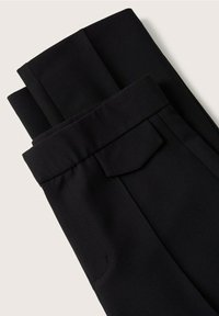 Pantalons noirs ajustés en tissu lisse, dotés d'un devant plat, de poches latérales et d'un ourlet à la cheville pour une silhouette structurée.
