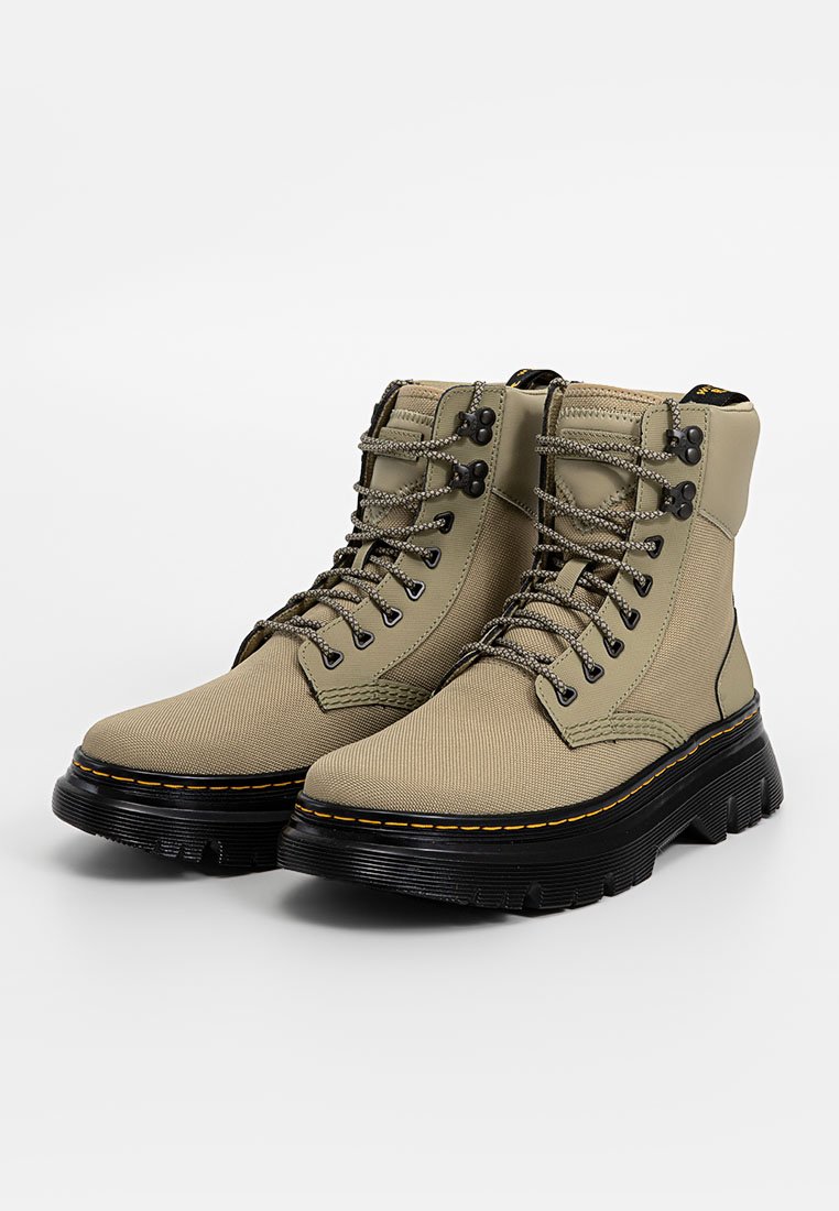 Bottes beiges en toile à lacets avec semelle en caoutchouc noire, semelle épaisse, œillets en métal et couture jaune contrastante sur la semelle intermédiaire.