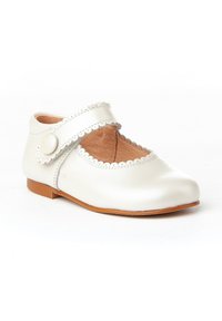 Zapato Mary Jane de cuero blanco con bordes festoneados y punta redonda, con una correa lateral con un botón y una suela de goma marrón.