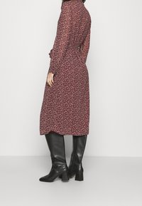 Lång, vinröd klänning med blommönster, midjeband och långa ärmar, kombinerad med knähöga svarta läderstövlar med klack.