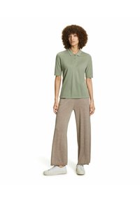 Olijfgroene polo met een kraag en drie knopen, gecombineerd met lichtbeige wijde broekspijpen. Witte sneakers maken de outfit compleet.
