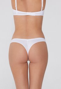 Weißer Tanga aus glattem Stoff, mit minimaler Abdeckung und einem schlichten Design, dünnen Trägern und einem nahtlosen Finish.