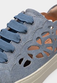Ανοιχτό μπλε τζιν αθλητικό παπούτσι με φαρδιές κορδόνια σε μπλε υφή και μοτίβα κοψίματος σε σχήμα λουλουδιού στο πλάι.