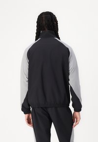 Black and light gray windbreaker jacket with a stand collar, elastic cuffs, and waistband. Features contrasting sleeves and smooth fabric.