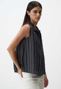 Blusa senza maniche di colore blu navy con strisce verticali bianche, con design colletto, in tessuto leggero e vestibilità rilassata, abbinata a pantaloni bianchi.