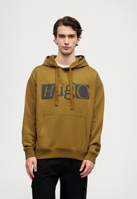 Olivgrüner Hoodie aus weichem Stoff, mit einer vorderen Kängurutasche, Kordelzug-Kapuze und einem schwarzen Grafiklogo auf der Brust.
