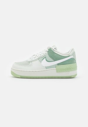 Niska trampki w białym i jasnym zielonym kolorze z białymi sznurowadłami, białym logo Nike oraz grubą podeszwą oznaczoną napisem "AIR" na pięcie.