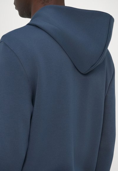 Felpa con cappuccio di colore blu scuro, caratterizzata da una texture liscia, una vestibilità comoda e un design minimalista. Cuciture visibili lungo i bordi.