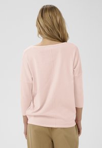 Pull oversize rose clair avec des manches aux trois quarts et un large décolleté. Tissu doux et texturé avec une couture centrale au dos.