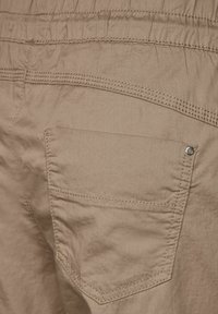 Pantalones color crema claro con cintura fruncida y bolsillo trasero. Presentan una textura sutil y un detalle de costura en contraste.