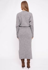 Szara dzianinowa sukienka swetrowa z długimi rękawami i prążkowaną fakturą, o dopasowanym kroju i dłuższym tylnym obrzeżu. W zestawieniu z brązowymi kozakami za kolano.