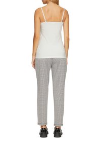 Wit mouwloos topje met dunne bandjes, gedragen met lichtgrijze geruite broek en zwarte schoenen met dikke zolen, bekeken vanaf de achterzijde.
