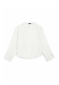 Camicia bianca a maniche lunghe con bottoni, decorata da ricami floreali testurizzati, colletto tondo e maniche con polsini, poggiata su uno sfondo bianco.