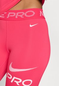 Rosa treningsleggings med en bred elastisk midje som har "PRO" i hvit skrift. Inkluderer en hvit Nike-logo på låret.