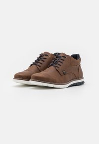 Brune lædersko med en tekstureret finish, prydet med runde snørebånd, guldøjer og en hvid gummisål med sorte detaljer.