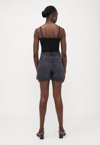 Pantalones cortos de mezclilla negra con una cintura alta, que cuentan con dos bolsillos traseros y un acabado limpio. La modelo lleva una camiseta sin mangas negra y sandalias de tacón.