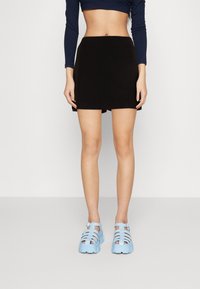 Černá mini sukně s hladkým povrchem, spárovaná se světle modrými sandály na platformě se zkříženými pásky, které mají robustní podrážku a detail s přezkou.