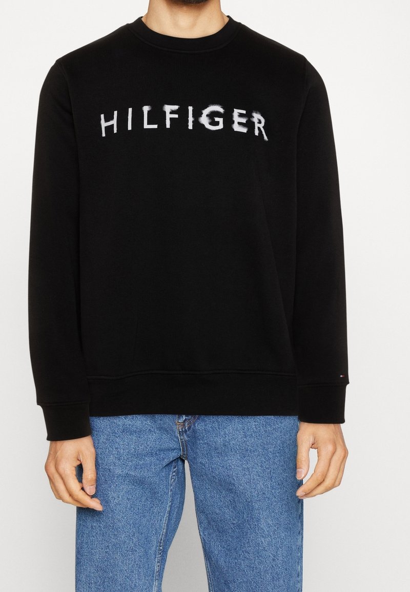Černá mikina s potiskem slova "HILFIGER" v opotřebovaném bílém písmu. Kulatý výstřih, dlouhé rukávy, žebrované manžety a spodní lem, vyrobená z měkké látky.