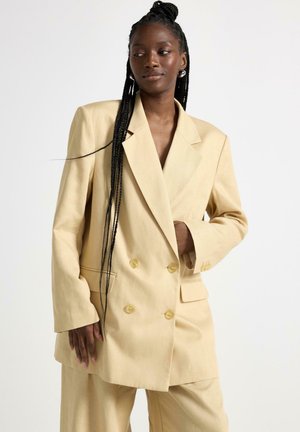 Kremfarvet dobbeltradet blazer med afslappet pasform, med store knapper og sidelommer, lavet af et let stof.