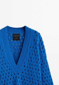 Niebieski sweter na drutach z dekoltem w kształcie litery V, ażurowym wzorem z motywem diamentów oraz prążkowanymi detalami wzdłuż kołnierza i dołu.