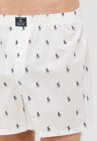 Boxeri din bumbac alb, cu un mic imprimeu cu jucători de polo în nuanțe de navy. Dispun de un brâu elastic și un eticheta cu logo țesut în față.