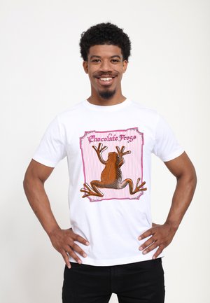 Bílý bavlněný tričko s ilustrací hnědé žáby a akcentními barvami růžové a fialové, s nápisem „Čokoládové žáby“.
