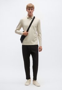 Μπεζ πόλο πουκάμισο με μακριά μανίκια, μαύροι στενοί παντελόνια και μπεζ αθλητικά παπούτσια, με μια μαύρη τσάντα ώμου για επιπλέον λεπτομέρεια.