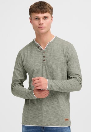 Langermige, vervaagde groene henley-shirt gemaakt van een gestructureerde stof, met een witte kraag en bruine knoopaccenten op de knoopsluiting.