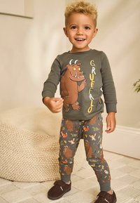Dark green sweatshirt featuring a Gruffalo illustration; gray patterned joggers with woodland animals; soft fabric; closed-toe slippers.