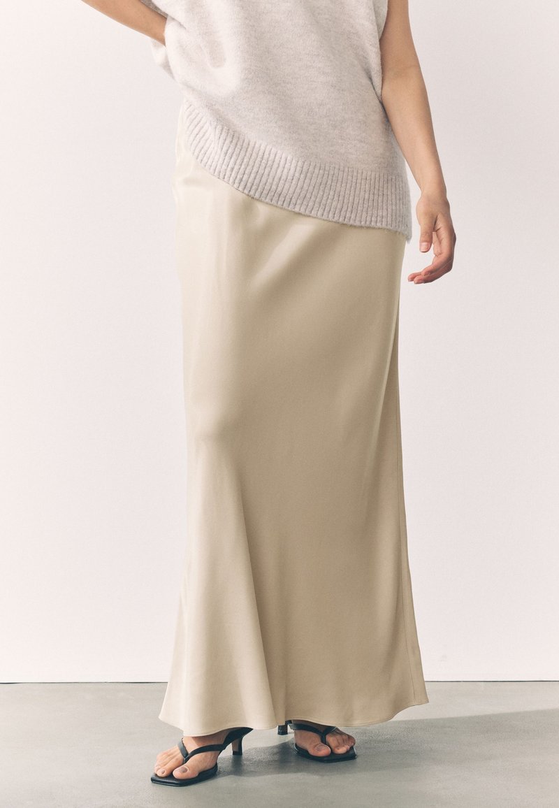 Lång, ljusbeige satinkjol med ett flödande mönster, kombinerad med en lös grå texturerad stickad topp och svarta sandaletter med klack.