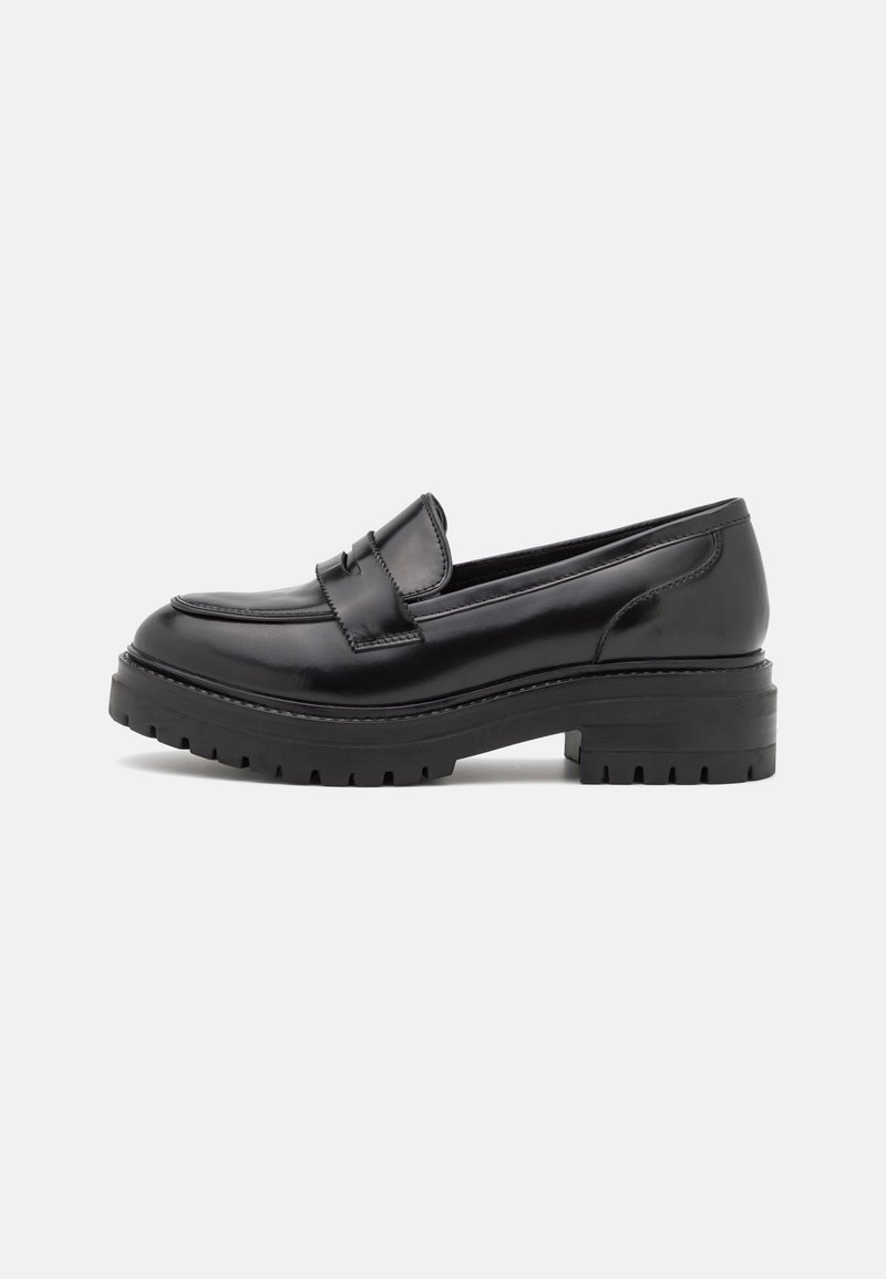 Mocassin en cuir noir avec semelle crantée épaisse et talon bas, présentant un design classique avec bride penny sur un fond uni.