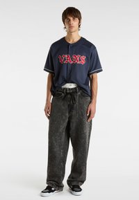 Marineblauwe baseballjersey met rode "VANS" letters, gecombineerd met losse, grijs acid-wash jeans en zwart-witte sneakers.