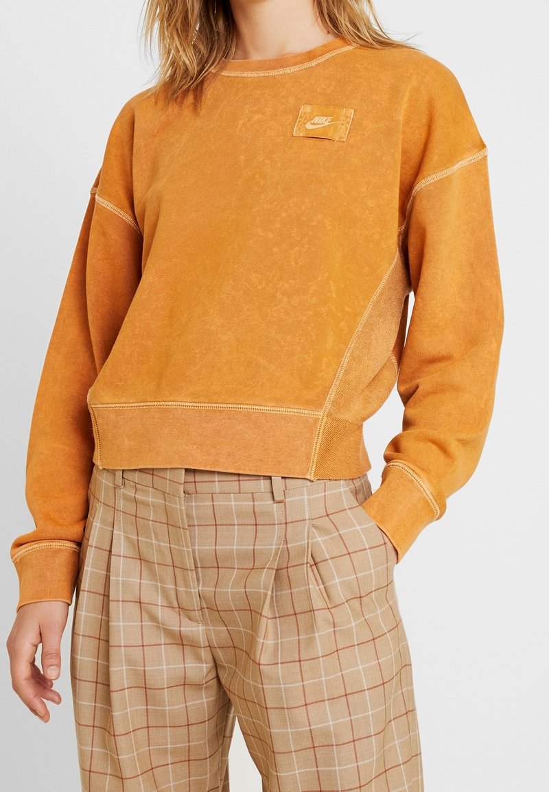 Oranget sweatshirt med en fyrkantig Nike-logotyp i en patch, ribbade ärmslut och nederkant. Tillsammans med beige rutiga byxor med bruna rutor.
