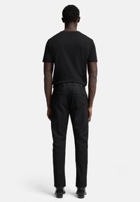Zwarte korte mouwen t-shirt gecombineerd met zwarte slim-fit broeken. De outfit heeft een klassiek ontwerp en een zachte textuur, geschikt voor casual draagstyles.